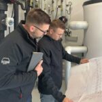 Zwei Techniker prüfen einen technischen Plan in einer Industrieanlage.