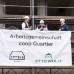 Drei Bauarbeiter mit Helmen bei einer Baustellenzeremonie mit Banner "Arbeitsgemeinschaft coop Quartier".