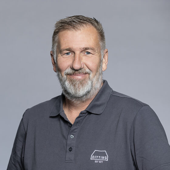 Porträt eines älteren Mannes mit grauem Bart, trägt dunkles Polo-Shirt mit "Ditting" Logo.