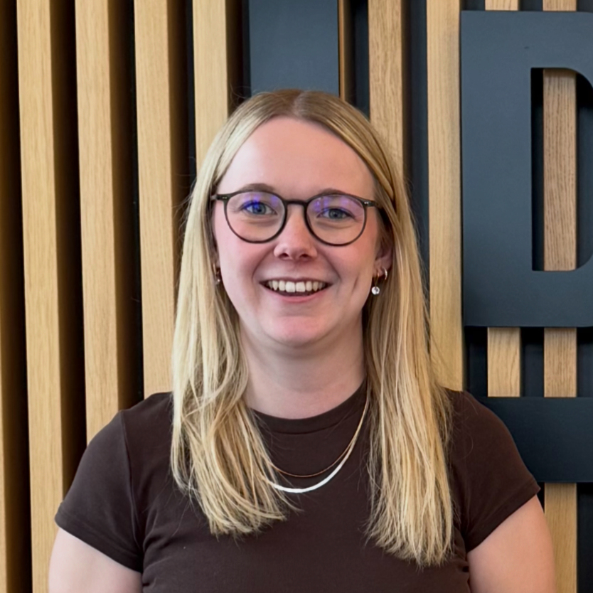 Lächelnde Frau mit Brille vor Holz- und blauer Wand im modernen Raum.