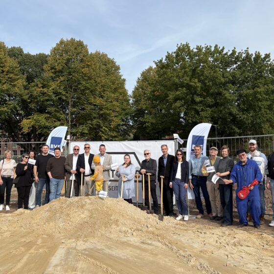 Gruppenfoto bei Baustart auf einer Baufläche mit Bäumen im Hintergrund.