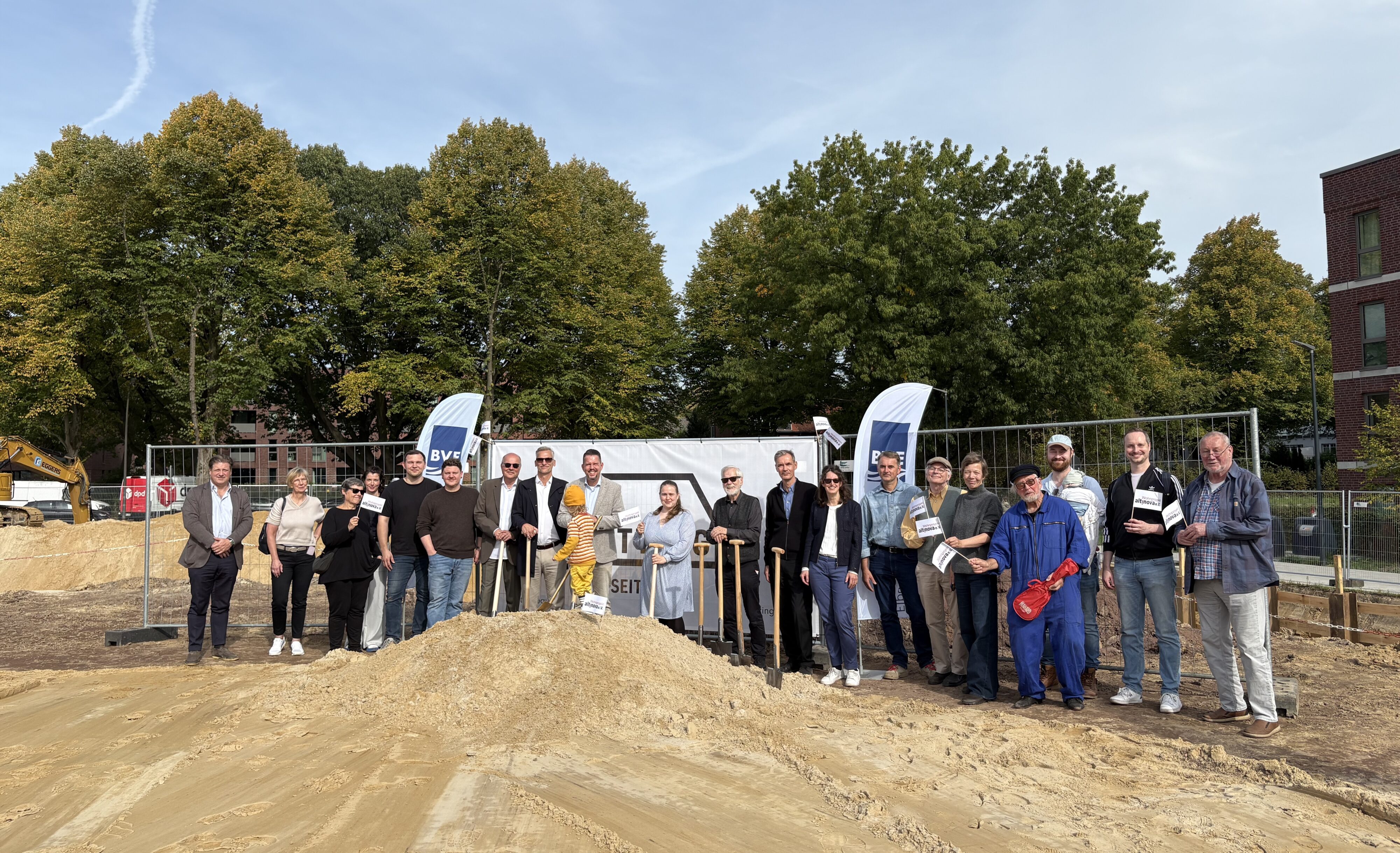 Gruppenfoto bei Baustart auf einer Baufläche mit Bäumen im Hintergrund.